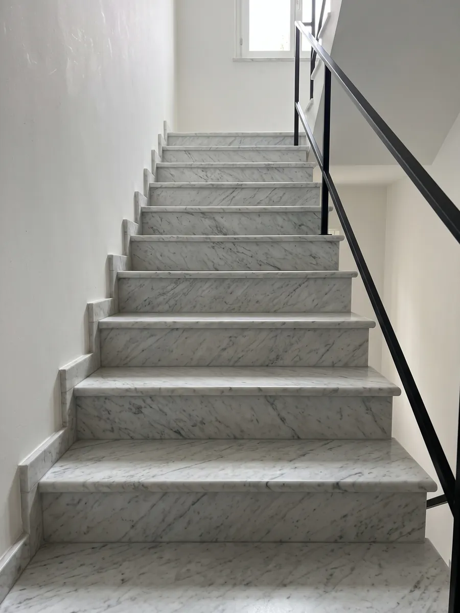 Interior staircase with white Carrara marble treads: grayish white with a fine, diffuse gray pattern spread across the whole surface