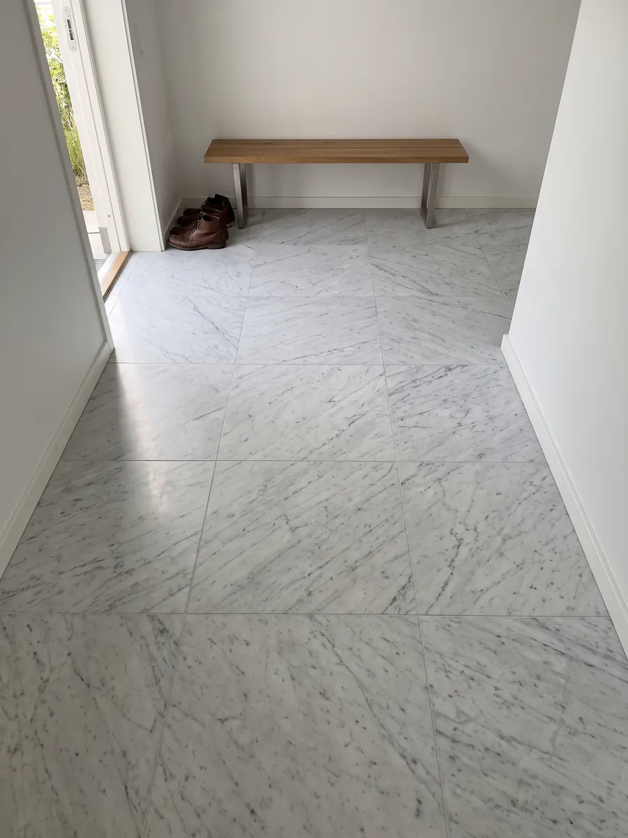 Entryway floor in large slabs of white Carrara marble: grayish white with a fine, diffuse gray pattern spread across the whole surface