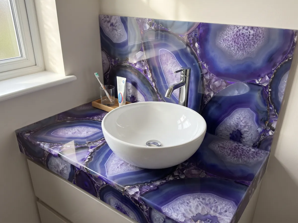 Vanity top and bathroom wall in Purple Agate with a white sink and chrome faucets: large slices of blue-violet agate with crystalline lilac centers