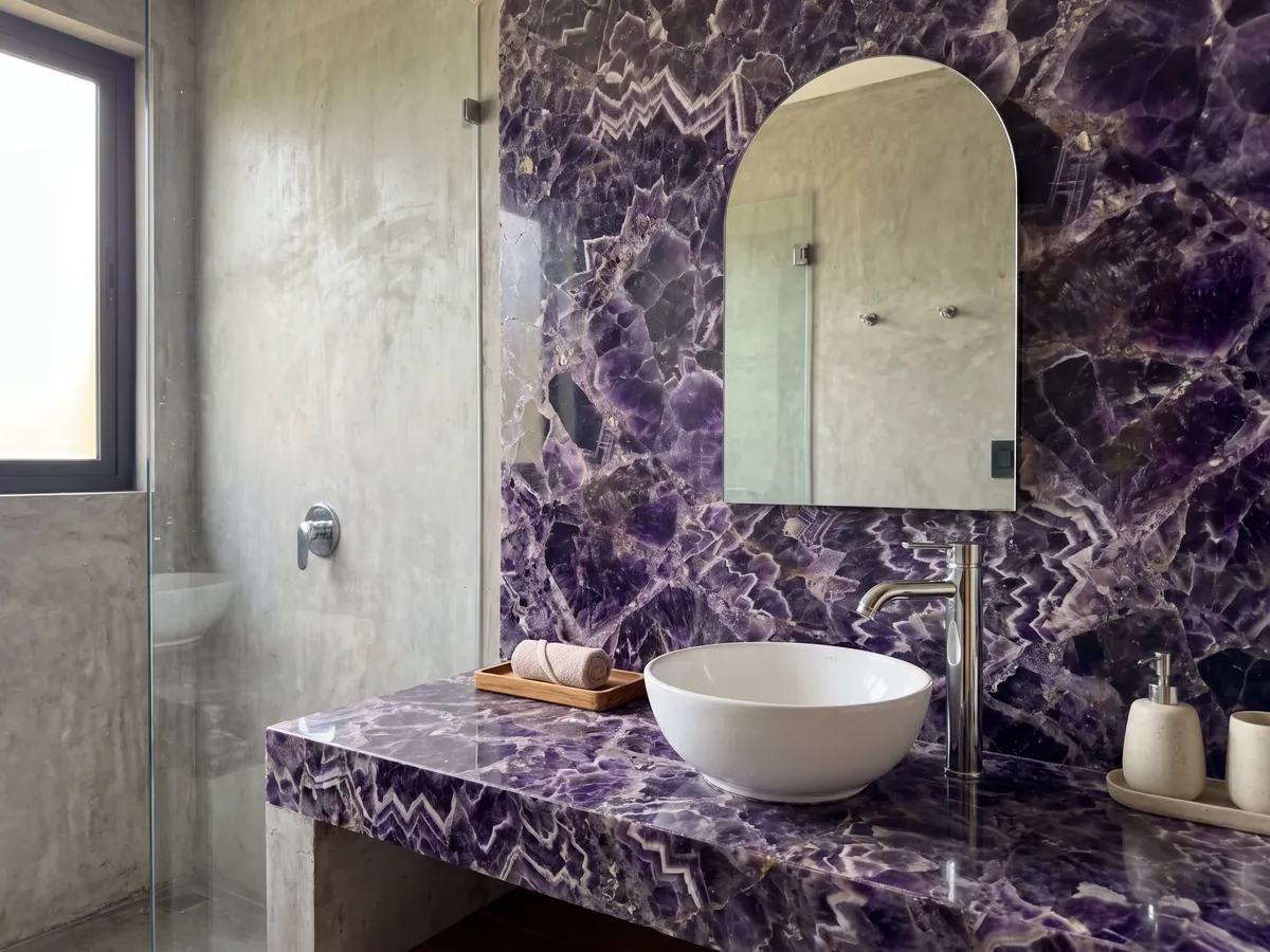 Vanity top and bathroom wall in amethyst with a white sink and chrome fittings: dark violet crystals with white and lilac zigzag bands