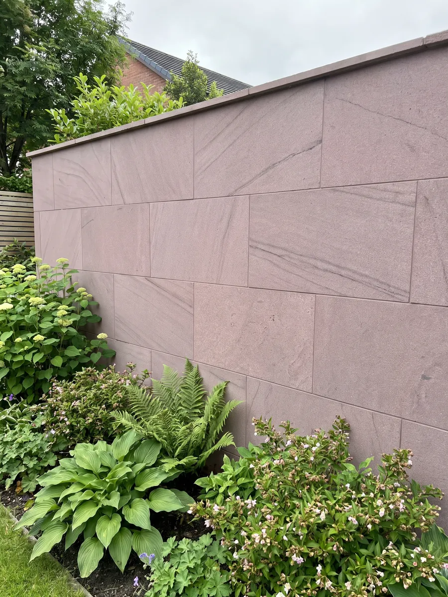Garden wall clad in Santafiora Brown sandstone with plants in front: an almost uniform mauve, fine-grained surface with no marked veins