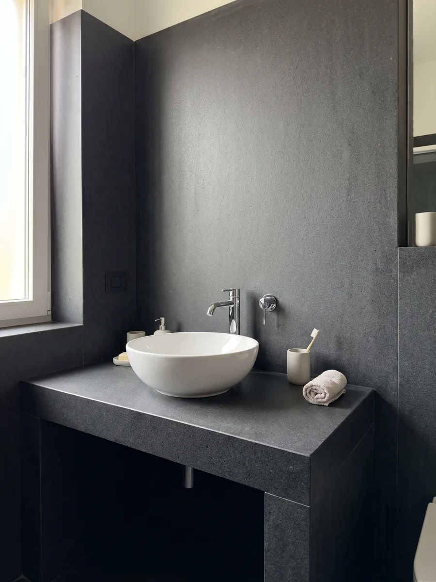 Vanity top and bathroom wall in Pietra Lavica basalt with a white sink and chrome faucets: almost black gray, uniform and very fine-grained