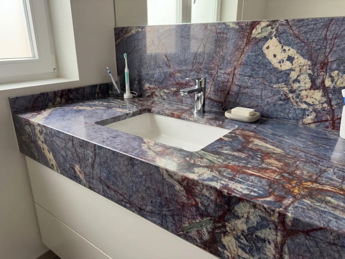 Vanity top and bathroom wall in Blue Luise quartzite with a white sink and chrome faucets: violet blue crossed by a dense network of rust red veins