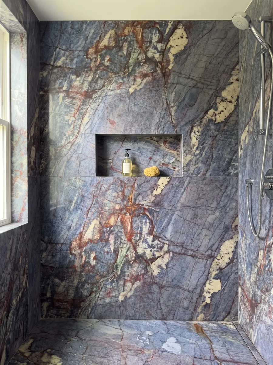Shower clad in full Blue Luise quartzite slabs with a recessed niche: violet blue crossed by a dense network of rust red veins