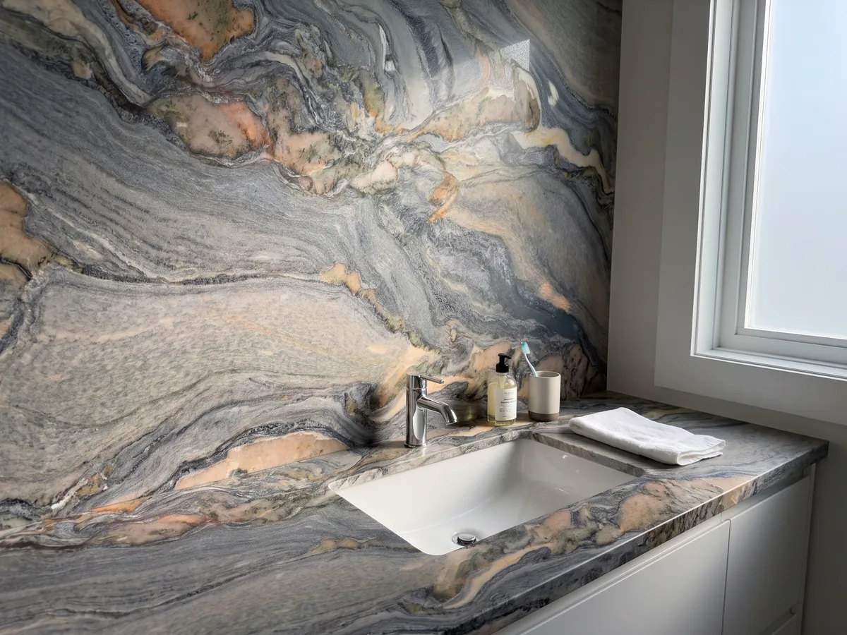 Vanity top and bathroom wall in blue Caravaggio quartzite with a white sink and chrome fixtures: blue-gray swirls with salmon and cream patches moving diagonally