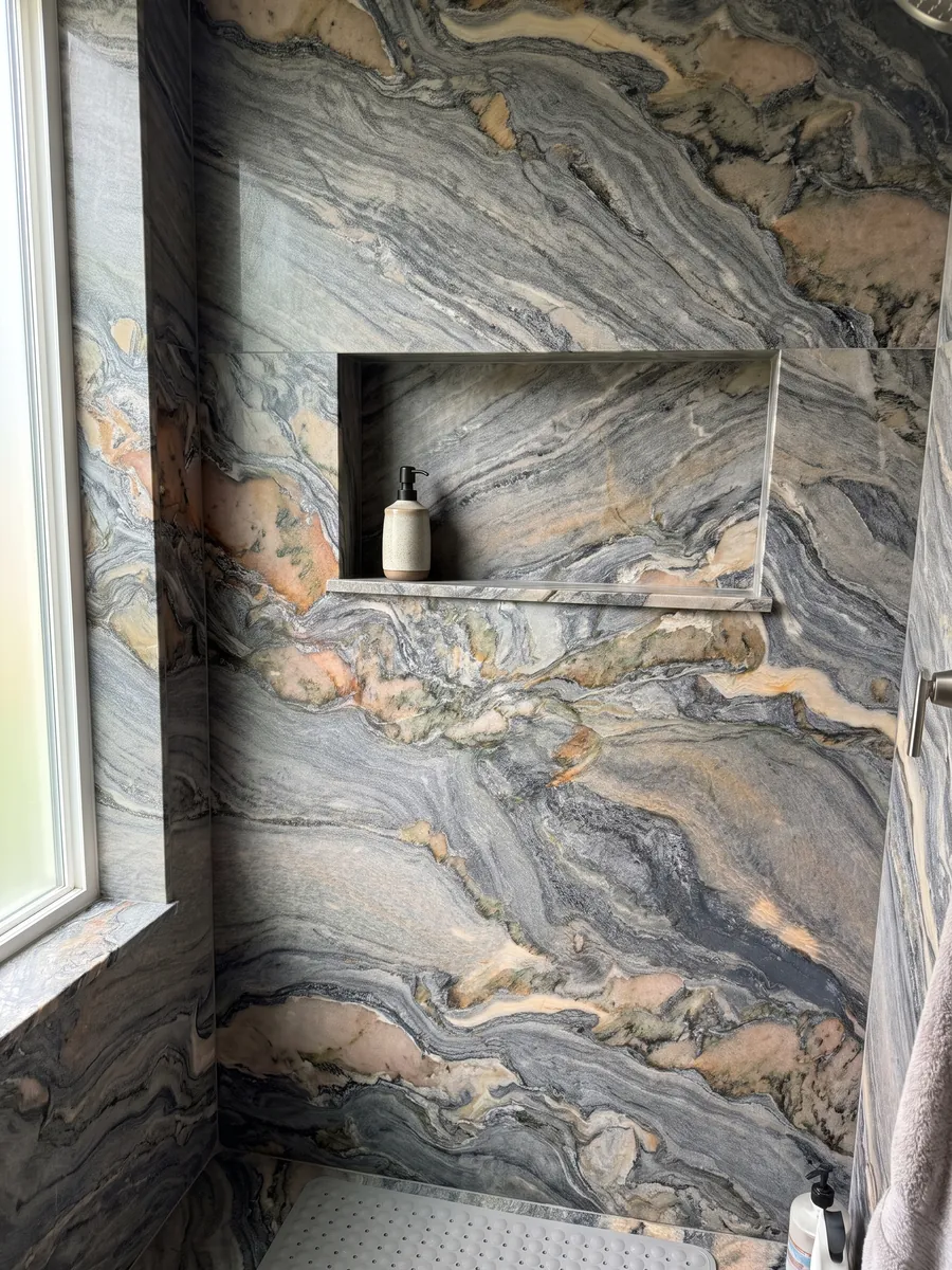 Shower clad in full blue Caravaggio quartzite slabs with a recessed niche: blue-gray swirls with salmon and cream patches moving diagonally