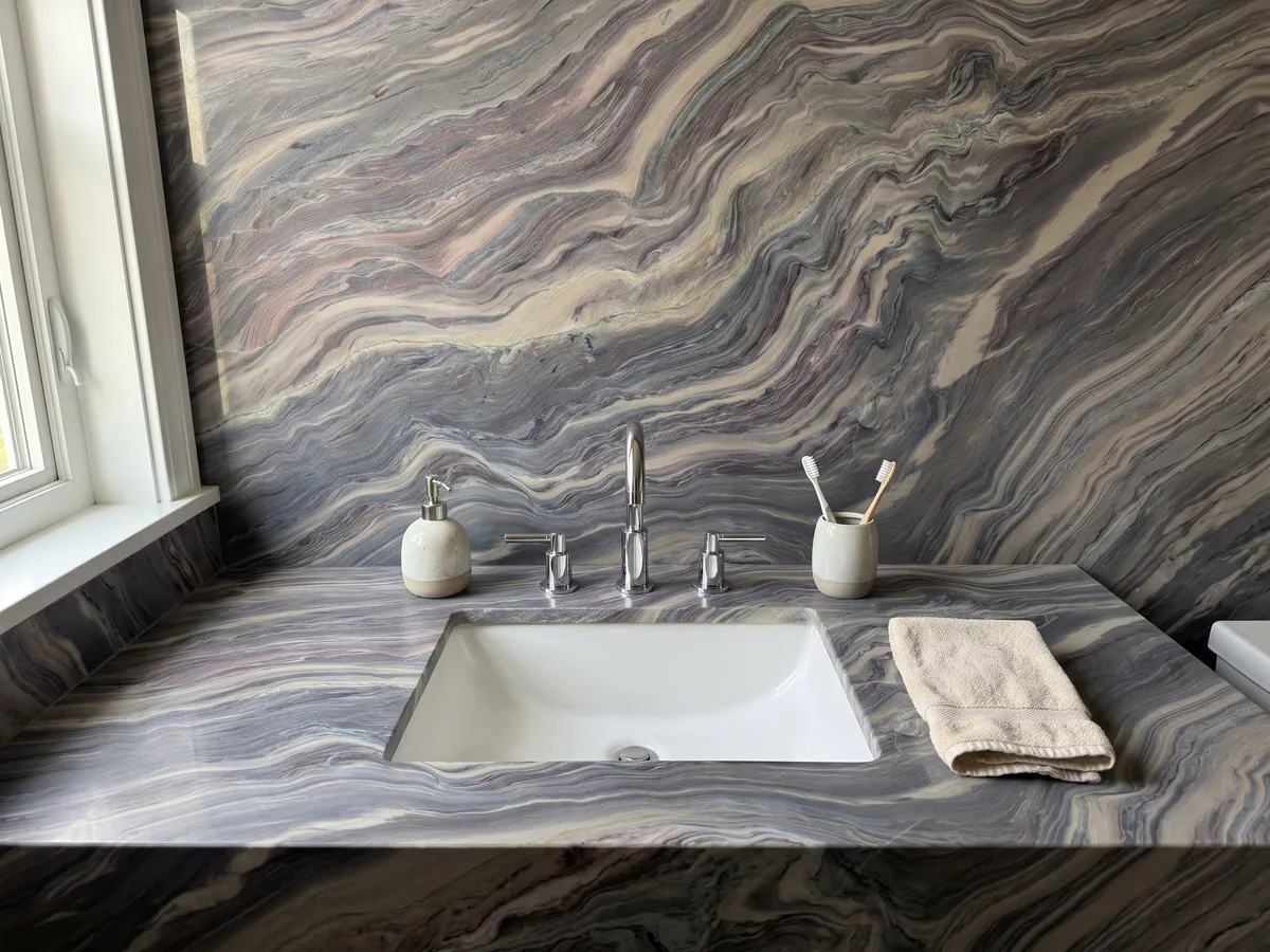 Vanity top and bathroom wall in Explosion Blue quartzite with a white sink and chrome faucet: tight blue grey and cream waves running across the whole slab on the diagonal