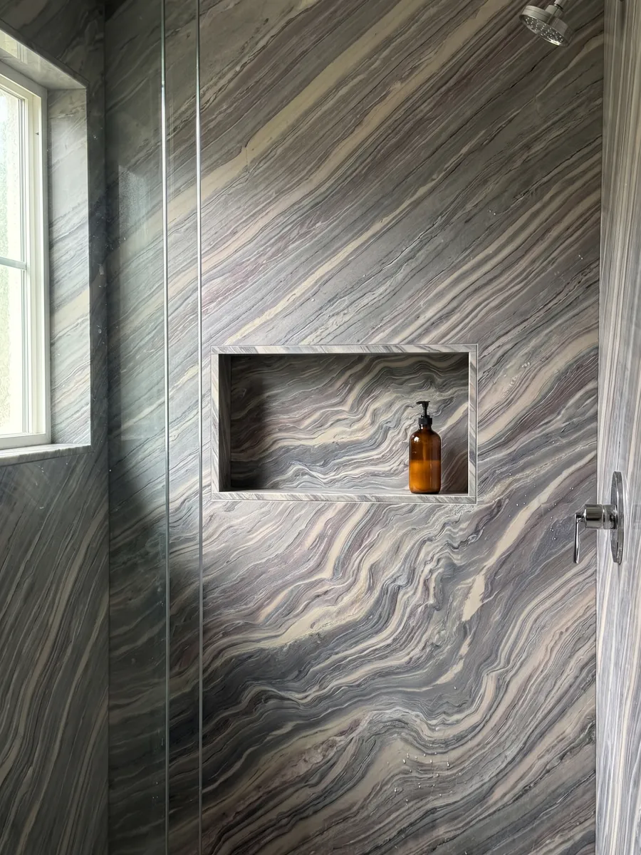 Shower clad in full slabs of Explosion Blue quartzite with a recessed niche: tight blue grey and cream waves running across the whole slab on the diagonal