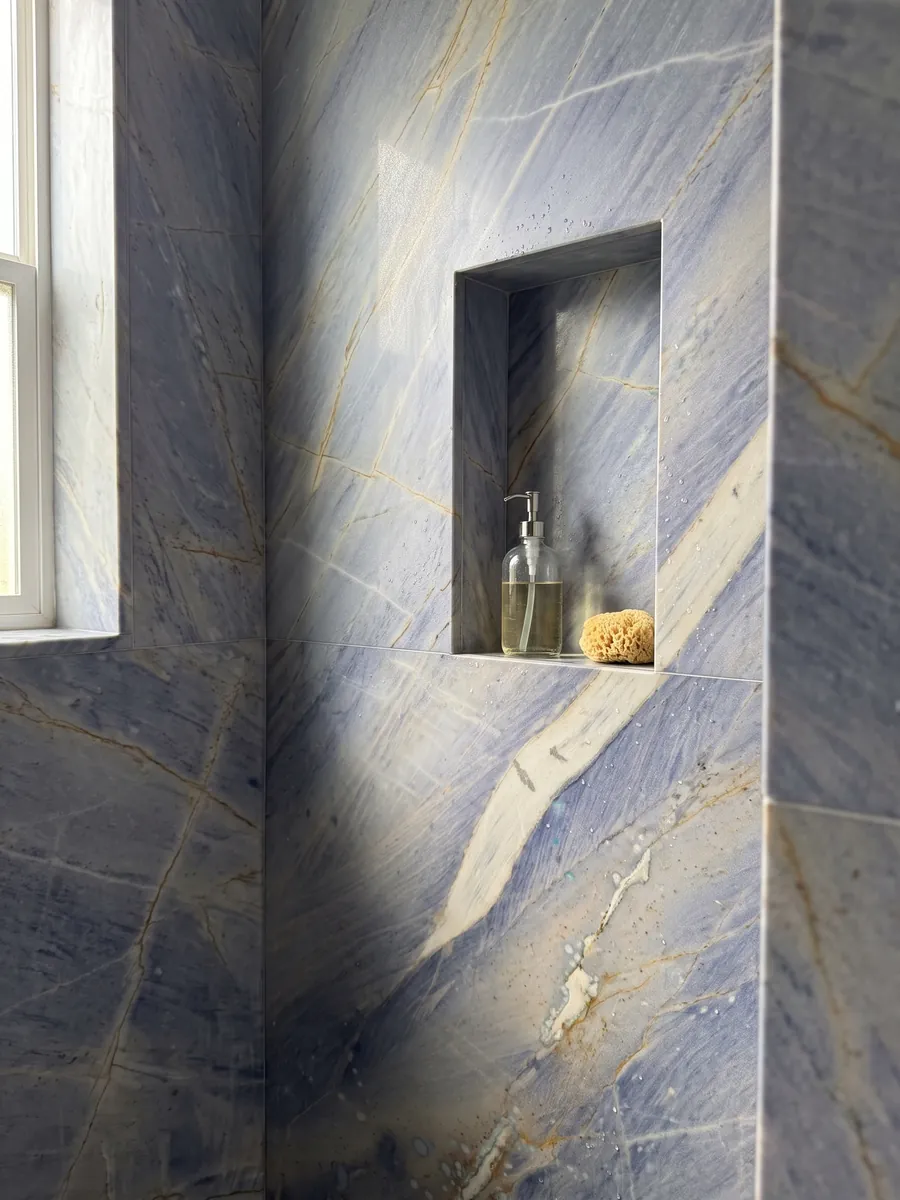 Shower clad in full Azul Macaubas quartzite slabs with a recessed niche: lavender blue background with a large cream band on the diagonal and ochre touches