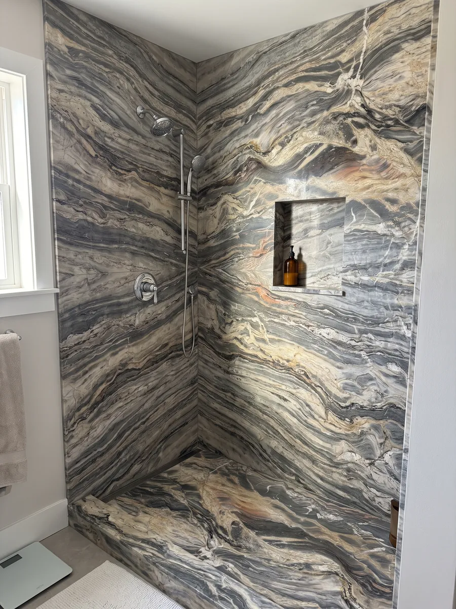 Shower clad in full beige Colorado quartzite slabs with a recessed niche: very busy horizontal waves in cream and dark gray, with the occasional orange touch