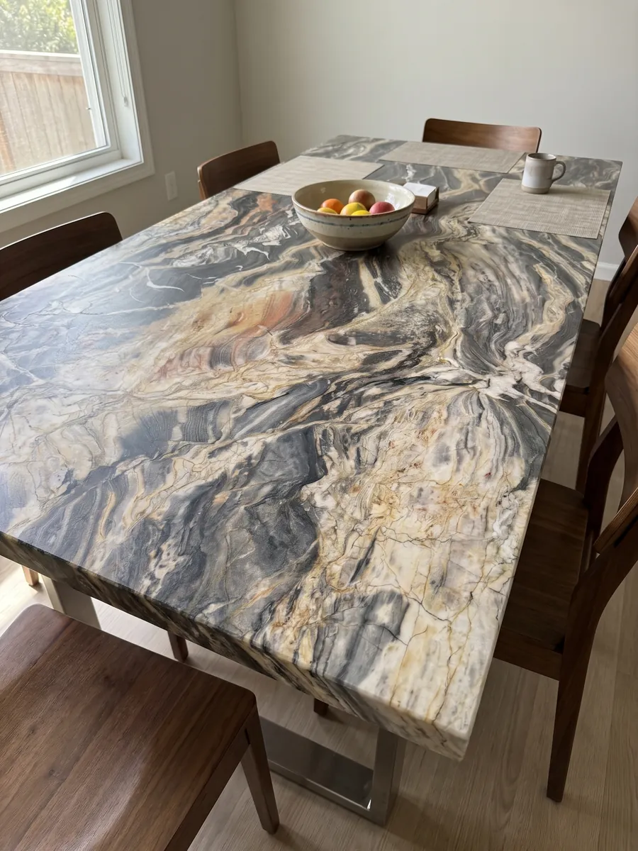Dining table with a beige Colorado quartzite top on a steel base: very busy horizontal waves in cream and dark gray, with the occasional orange touch