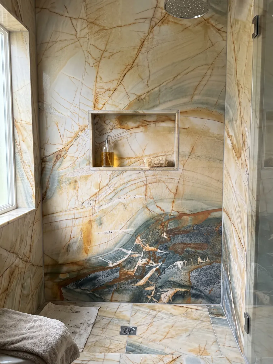 Shower clad in full beige Polaris Gold quartzite slabs with a recessed niche: cream and ochre with a net of orange veins and a lower petrol gray zone