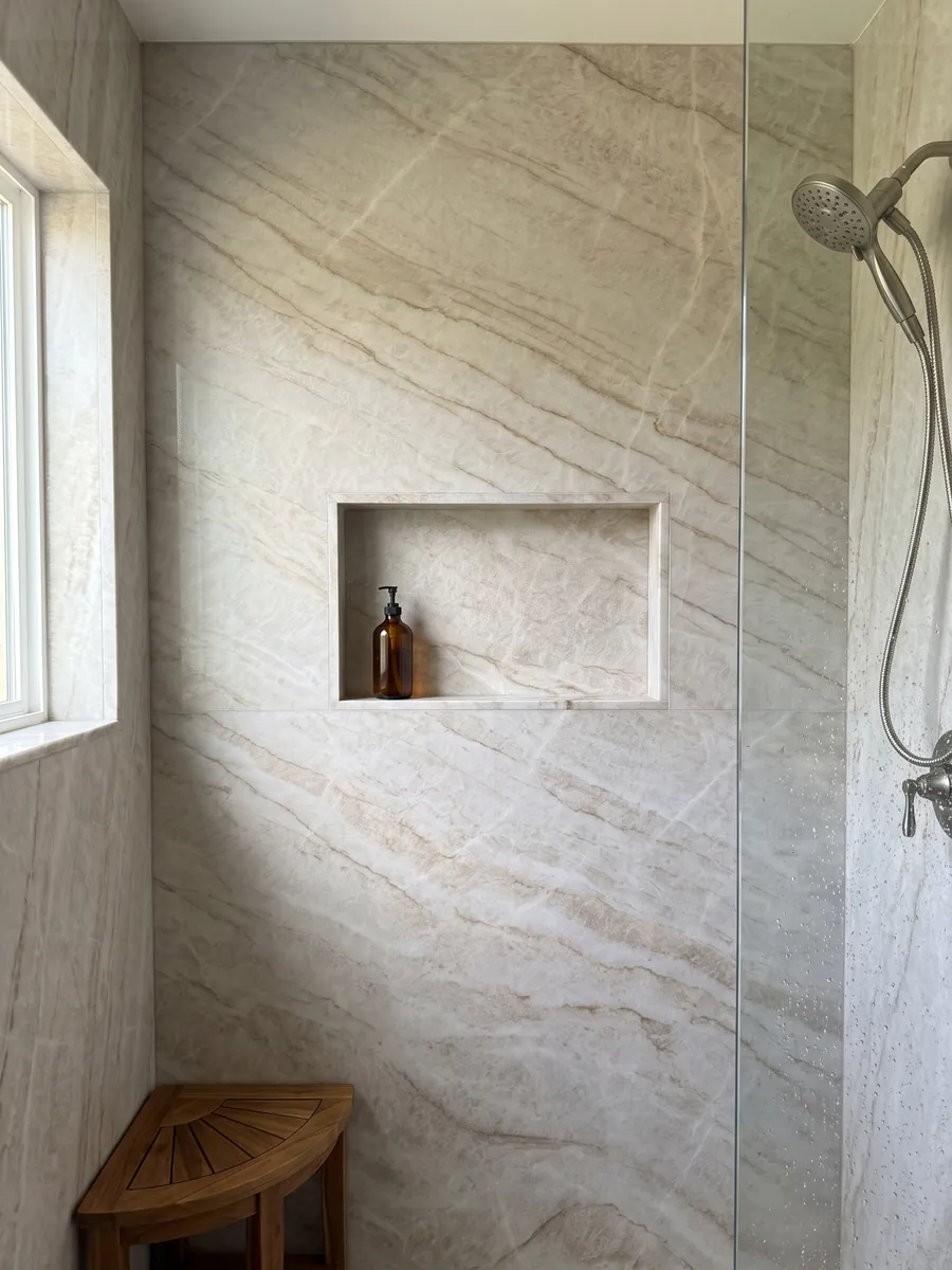 Shower clad in full slabs of beige Taj Mahal quartzite with a recessed niche: light beige with soft caramel veins in a diagonal