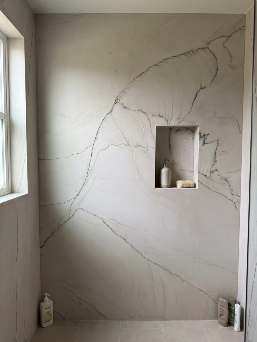 Shower clad in full slabs of white Dune quartzite with a recessed niche: bone white with a fine dark line tracing one large curve