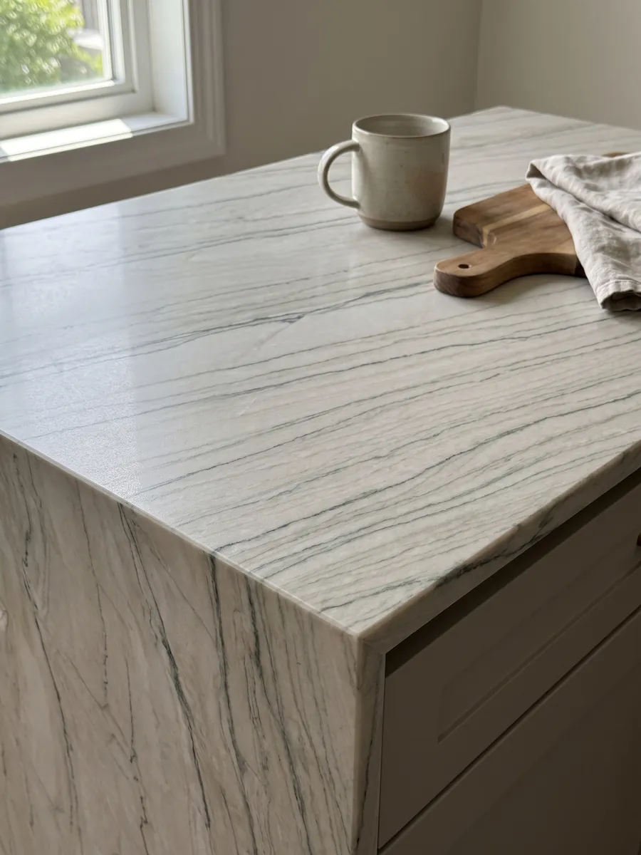 Straight edge of a white Macaubas Fantasy quartzite kitchen countertop with the veining continuing over the edge: creamy white with fine horizontal gray-green lines