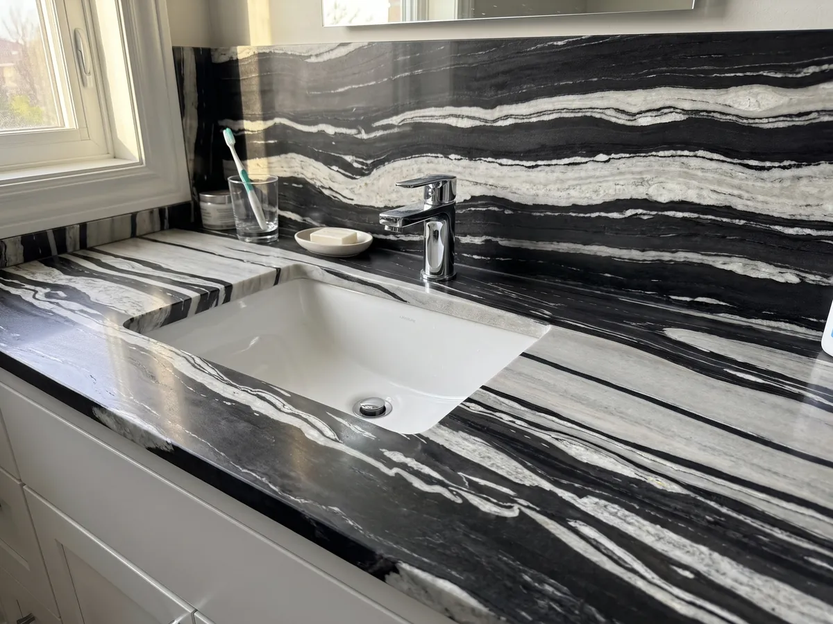Bathroom vanity top and wall in White Copacabana quartzite with a white sink and chrome faucet: alternating horizontal white and black bands of high contrast