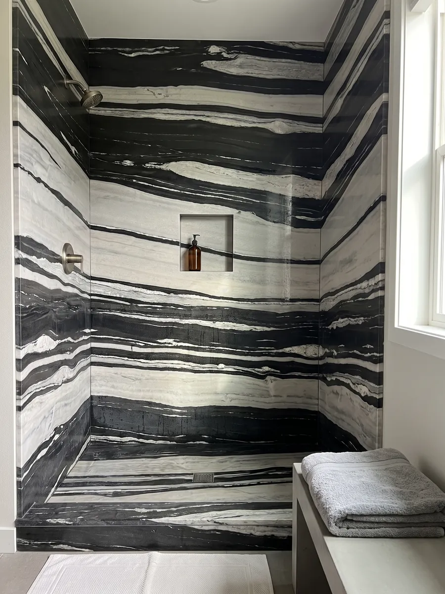 Shower clad in full White Copacabana quartzite slabs with a recessed niche: alternating horizontal white and black bands of high contrast