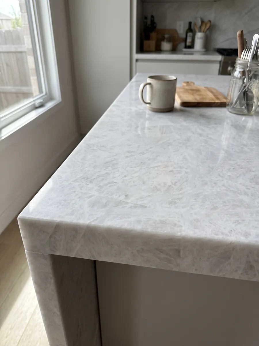 Straight edge of a kitchen countertop in grey Cristallo quartzite with the veining running over the edge: near-uniform greyish white with a soft crystalline look