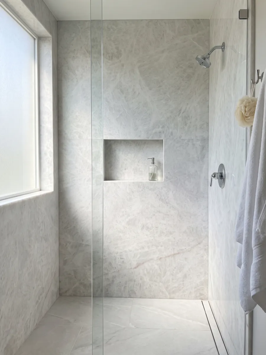 Shower clad in full grey Cristallo quartzite slabs with a recessed niche: near-uniform greyish white with a soft crystalline look