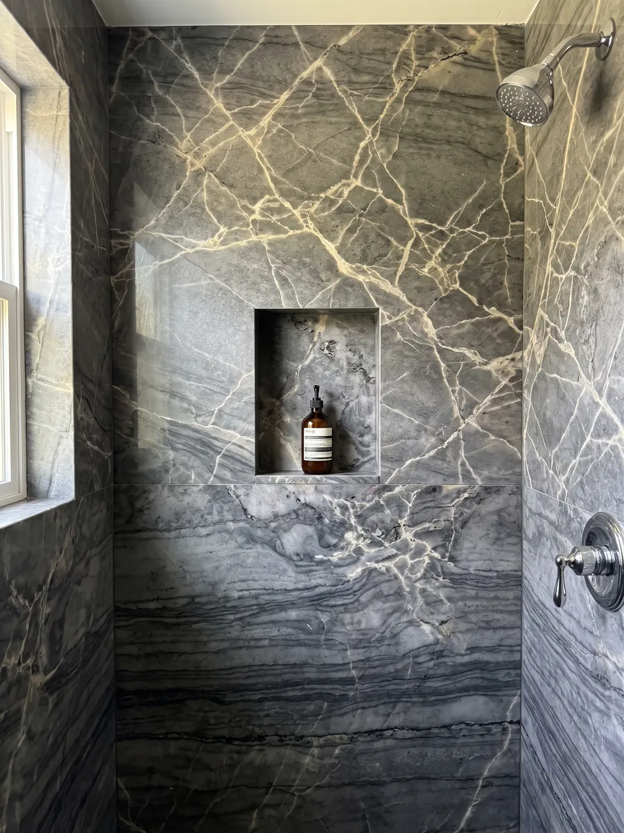 Shower clad in full London Grey quartzite slabs with a recessed niche: charcoal grey with a network of cream veins and dark horizontal waves