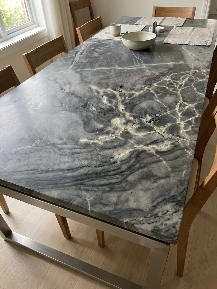 Dining table with a London Grey quartzite top on a steel base: charcoal grey with a network of cream veins and dark horizontal waves