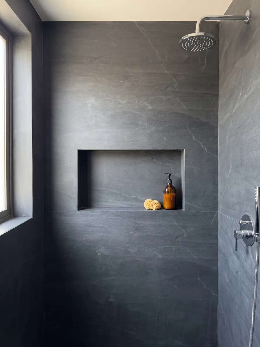 Shower clad in full slabs of gray Pietra del Cardoso quartzite with a recessed niche: uniform dark slate gray, no pattern