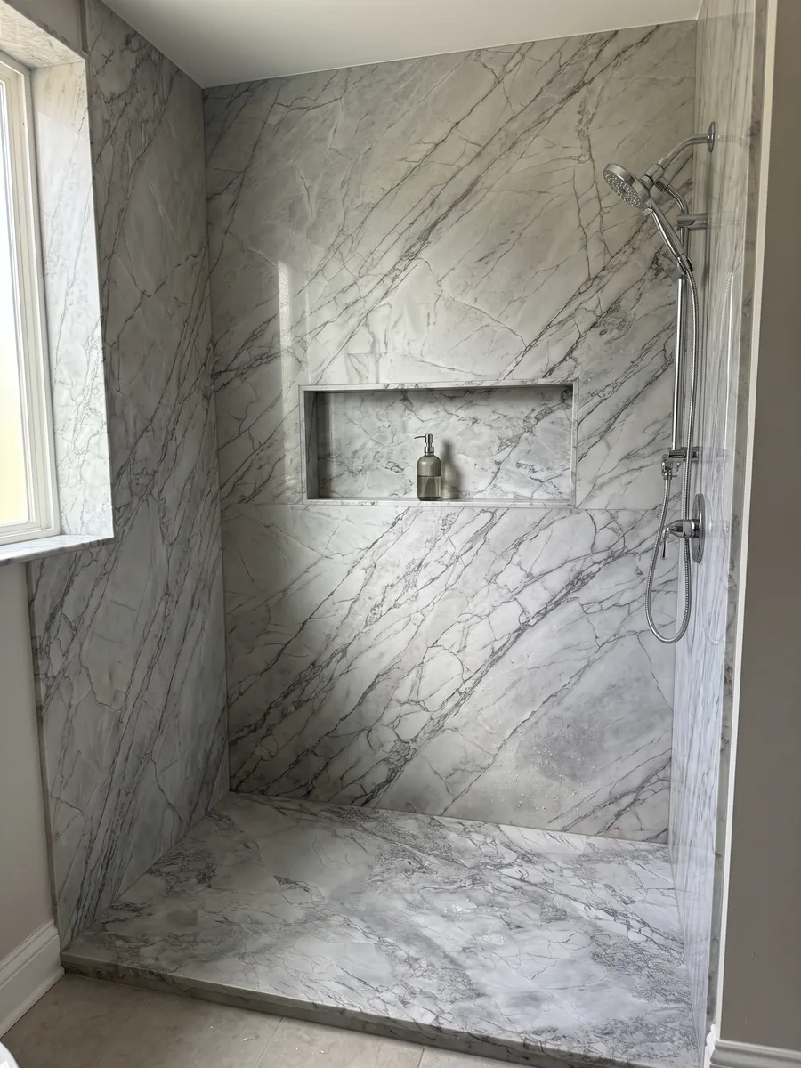 Shower clad in full slabs of gray Super White quartzite with a recessed niche: light gray with a network of slightly darker gray veins