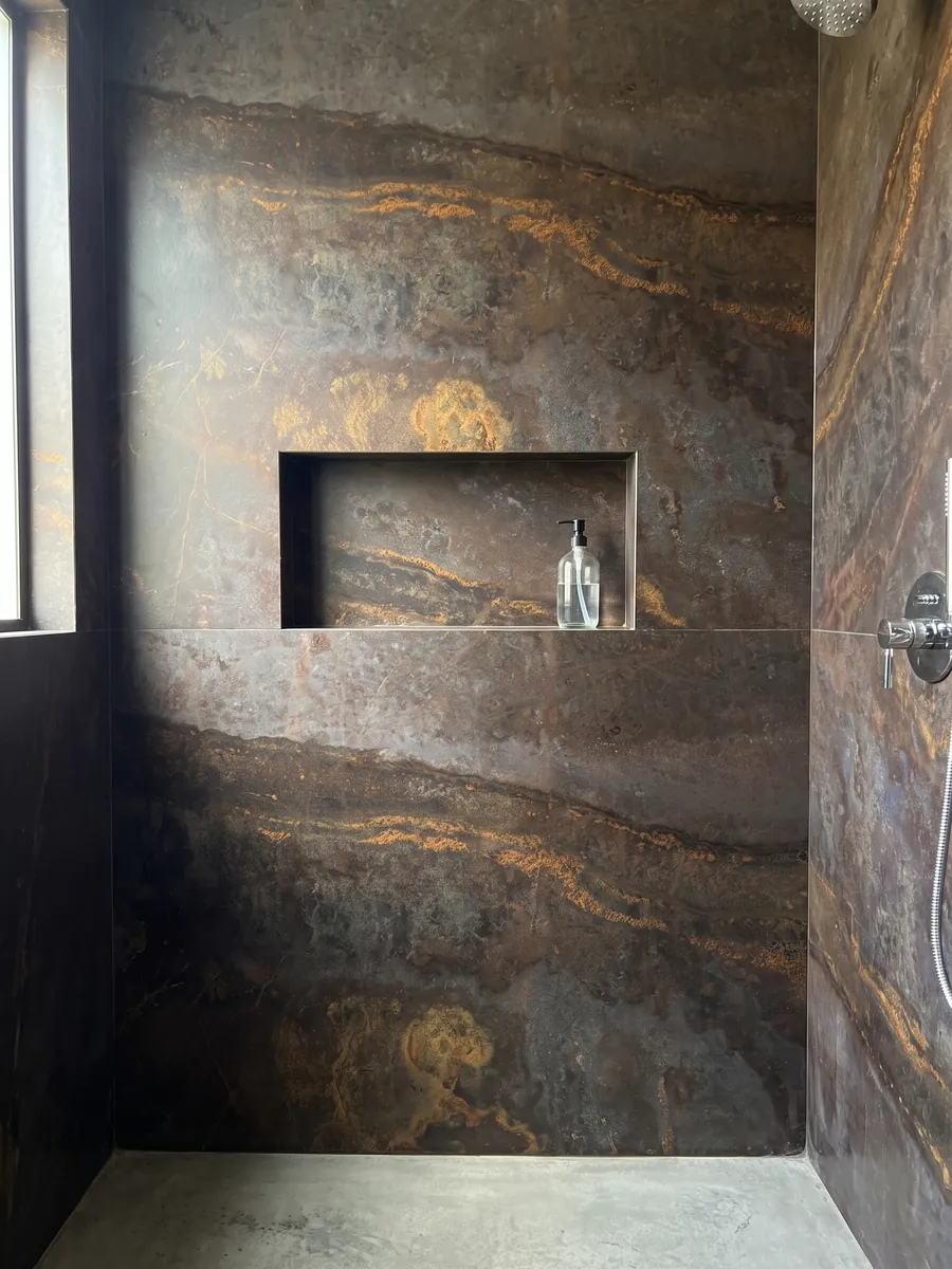 Shower clad in full brown Bronzite quartzite slabs with a recessed niche: dark brown with a horizontal band scattered with golden orange flecks