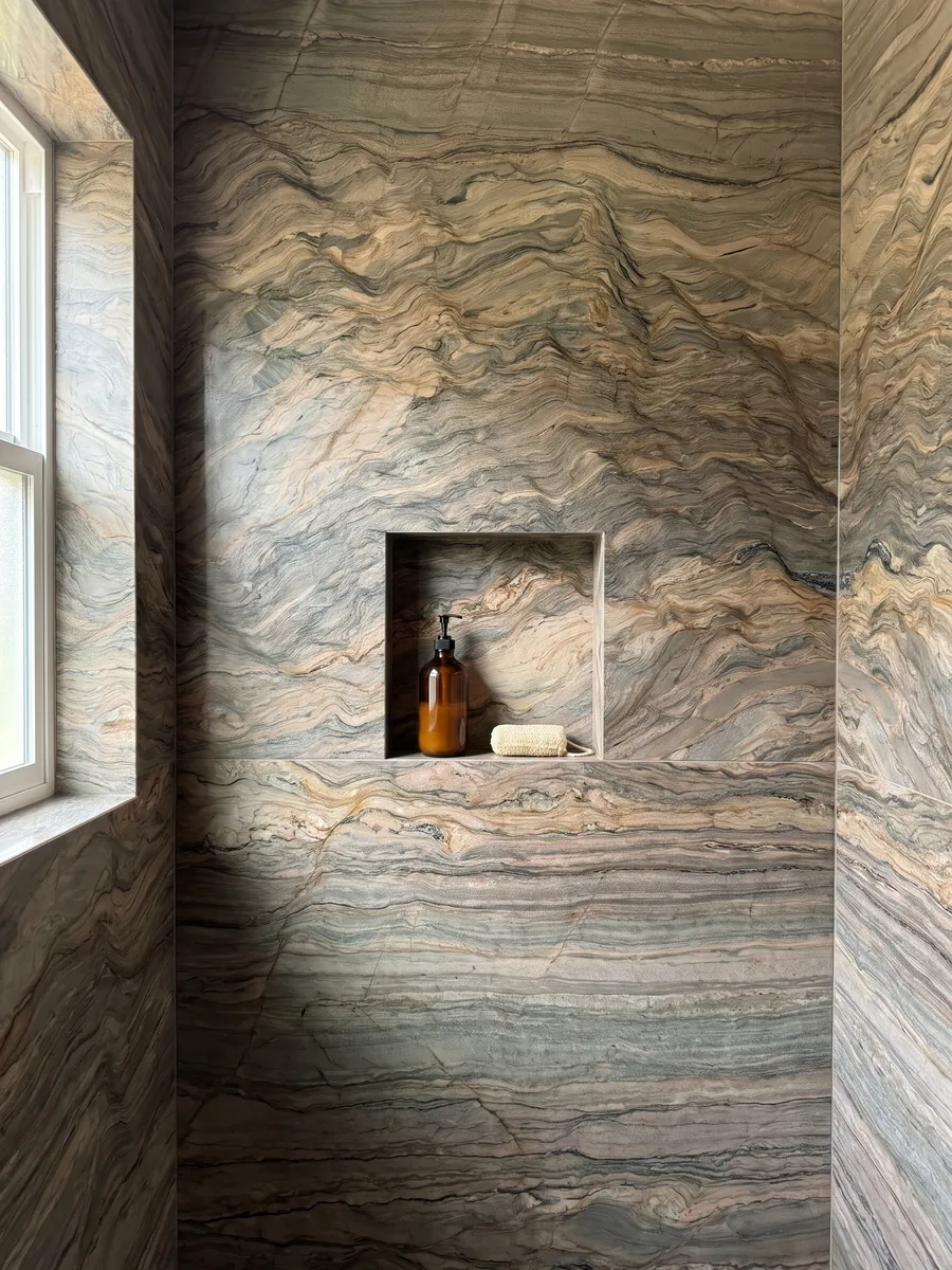 Shower clad in full slabs of brown Fusion quartzite with a recessed niche: horizontal waves in ocher and greenish gray, like layers of earth