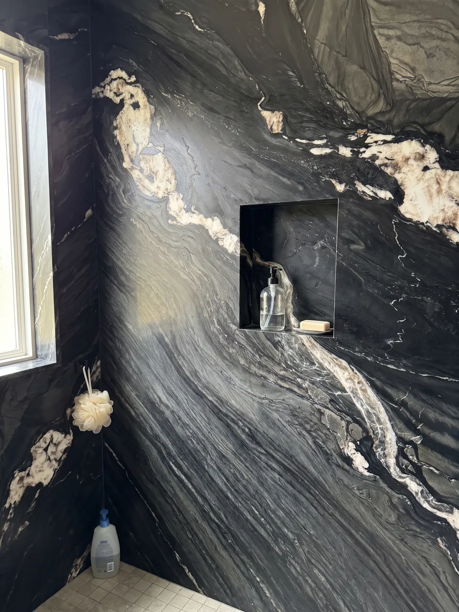 Shower clad in full Black Tempest quartzite slabs with a recessed niche: black with gray waves and a diagonal line of large white patches