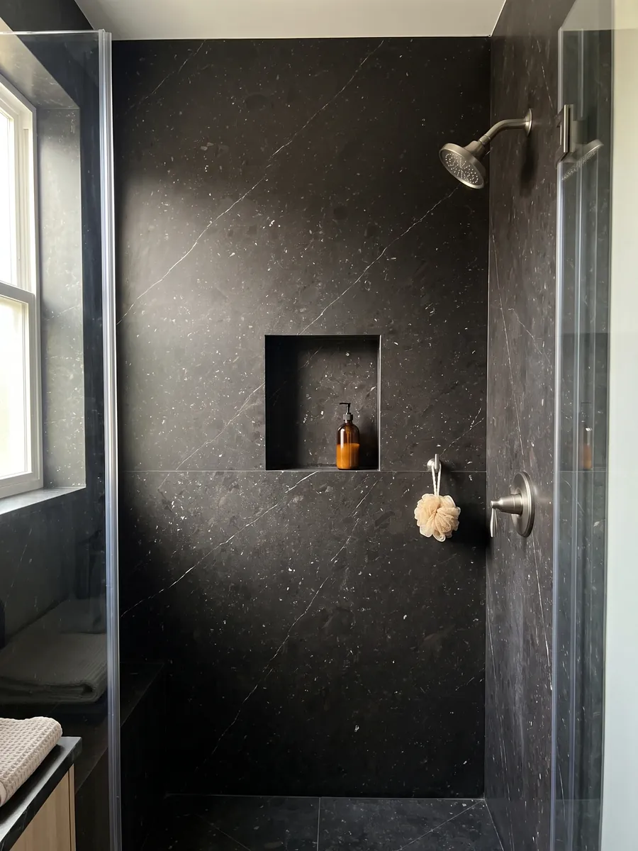 Shower clad in full black Infinity Brown quartzite slabs with a recessed niche: near black with fine diagonal white veins and light flecks