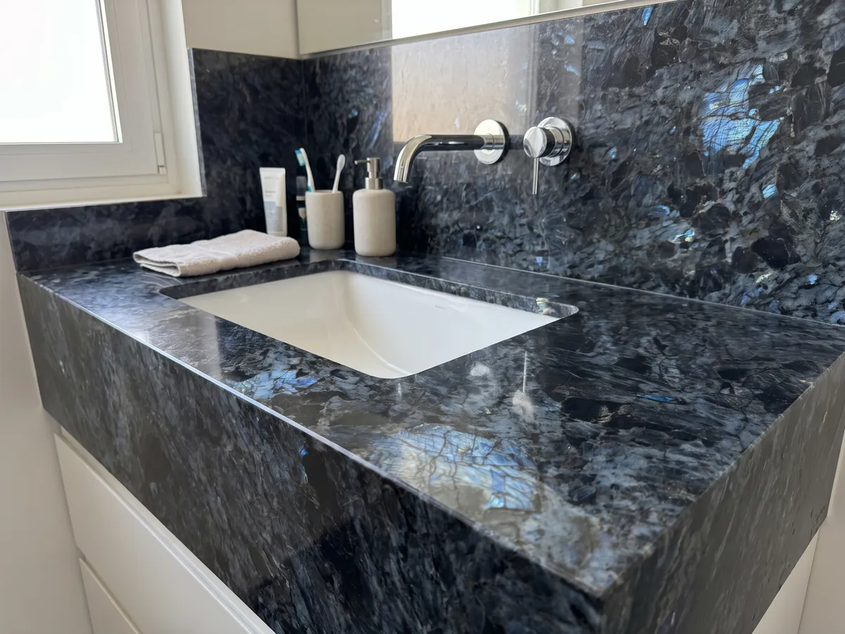 Vanity top and bathroom wall in Lemurian black quartzite with a white sink and chrome faucets: black with large crystals and flashes of iridescent blue