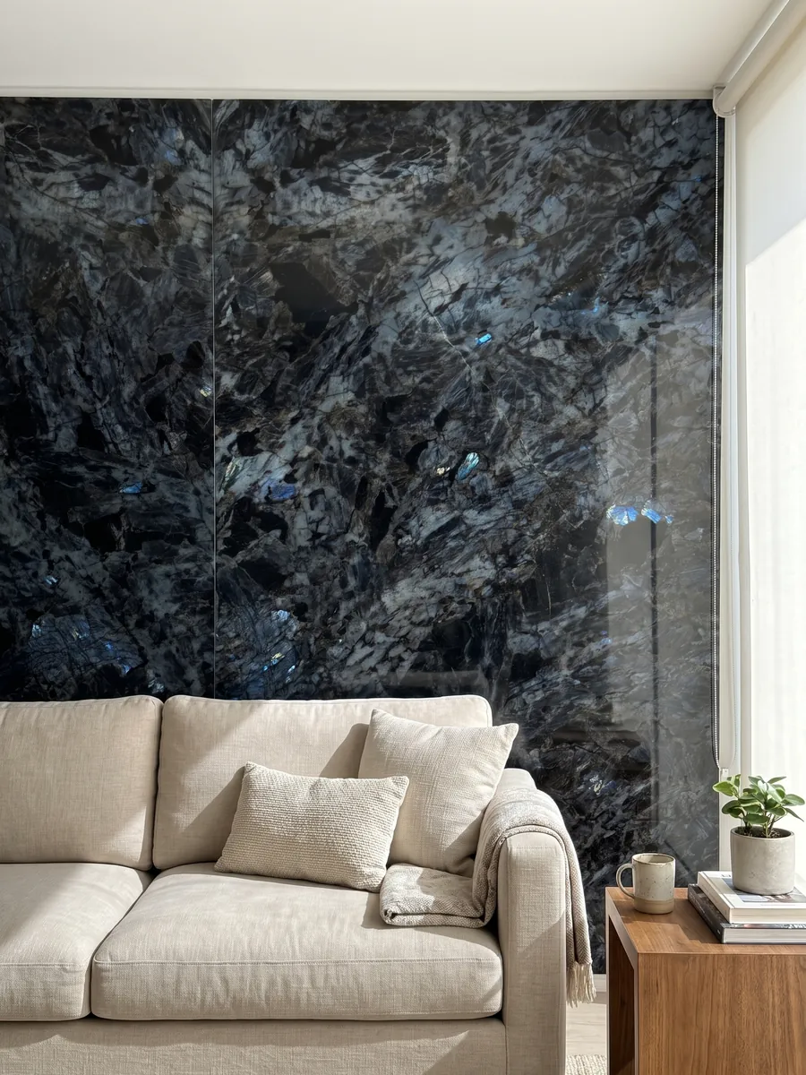 Living room wall clad in bookmatched Lemurian black quartzite slabs behind a sofa: black with large crystals and flashes of iridescent blue