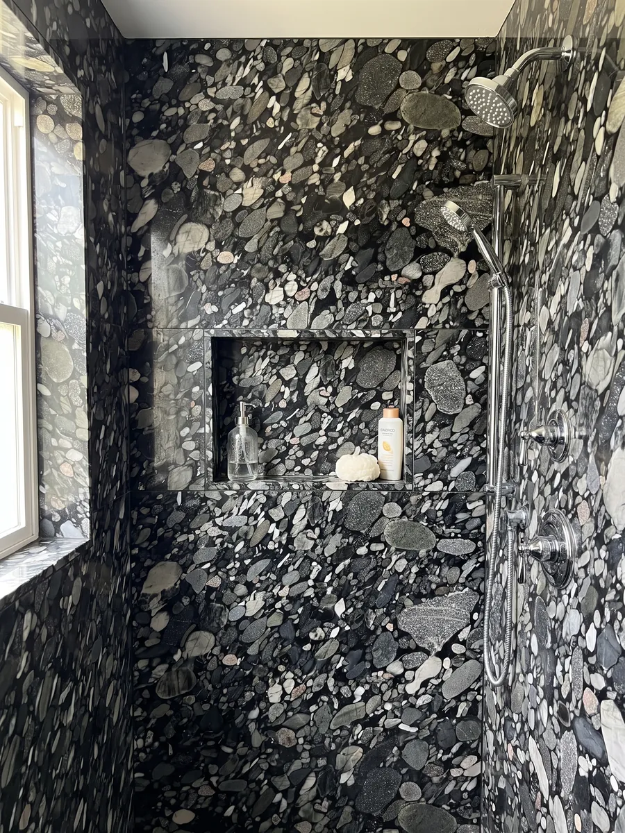 Shower clad in full slabs of Marinace Black quartzite with a recessed niche: tightly packed gray, white and black pebbles on a black background