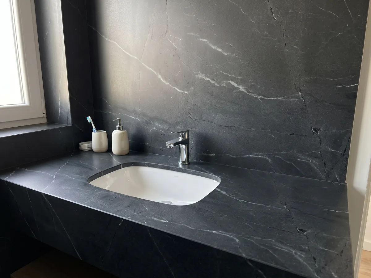 Vanity top and bathroom wall in Negresco black quartzite with a white sink and chrome faucets: black with fine, sparse diagonal white veins