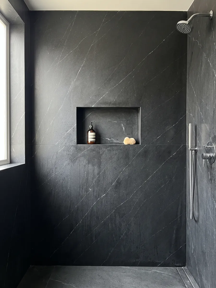 Shower clad in full Negresco black quartzite slabs with a recessed niche: black with fine, sparse white veins running diagonally