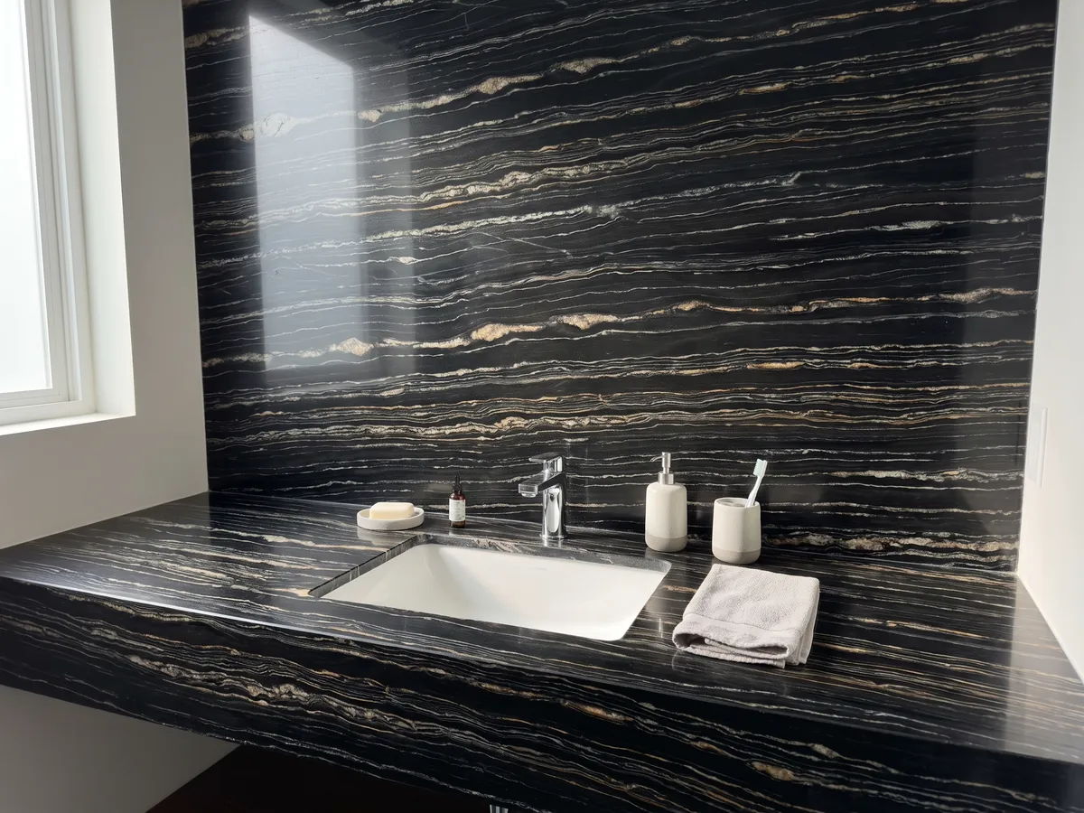 Bathroom vanity top and wall in Tropical Storm black quartzite with a white sink and chrome fixtures: black with fine horizontal white and gold lines