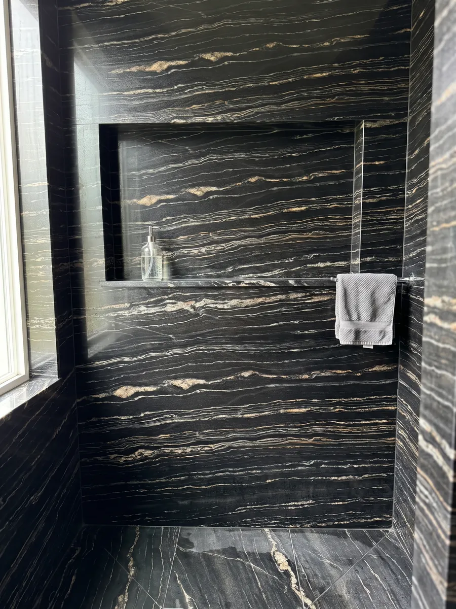 Shower clad in full Tropical Storm black quartzite slabs with a recessed niche: black with fine horizontal white and gold lines