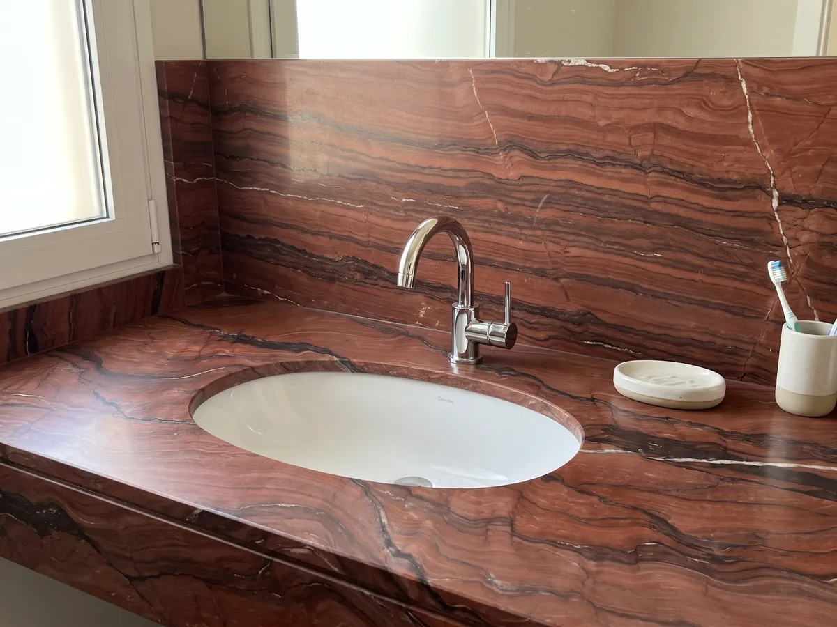 Vanity top and bathroom wall in Fusion Red quartzite with a white sink and chrome fixtures: brick red with horizontal dark waves and a thin white vein