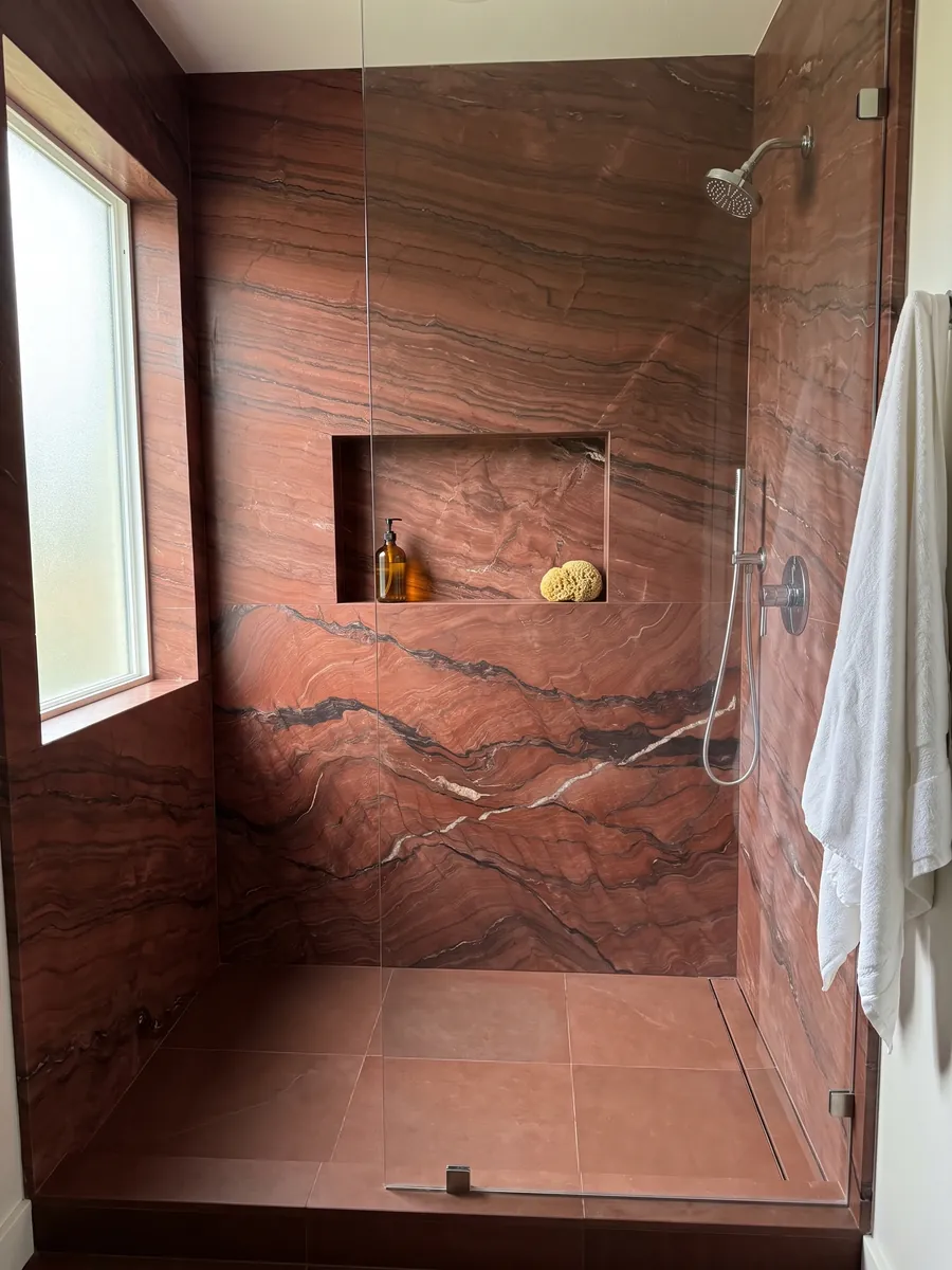 Shower clad in full slabs of Fusion Red quartzite with a recessed niche: brick red with dark horizontal waves and a thin white vein