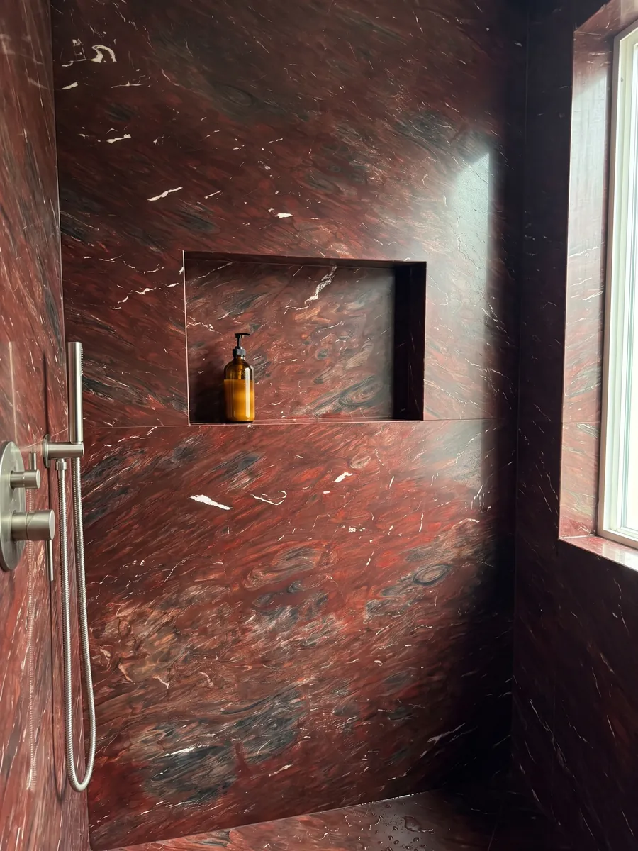 Shower clad in full Napoleon Bordeaux red quartzite slabs with a recessed niche: intense wine red with dark areas and small white streaks