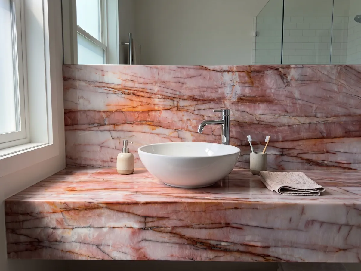Vanity top and bathroom wall in pink Juliet quartzite with a white sink and chrome faucets: intense pink and white with horizontal rust red veins