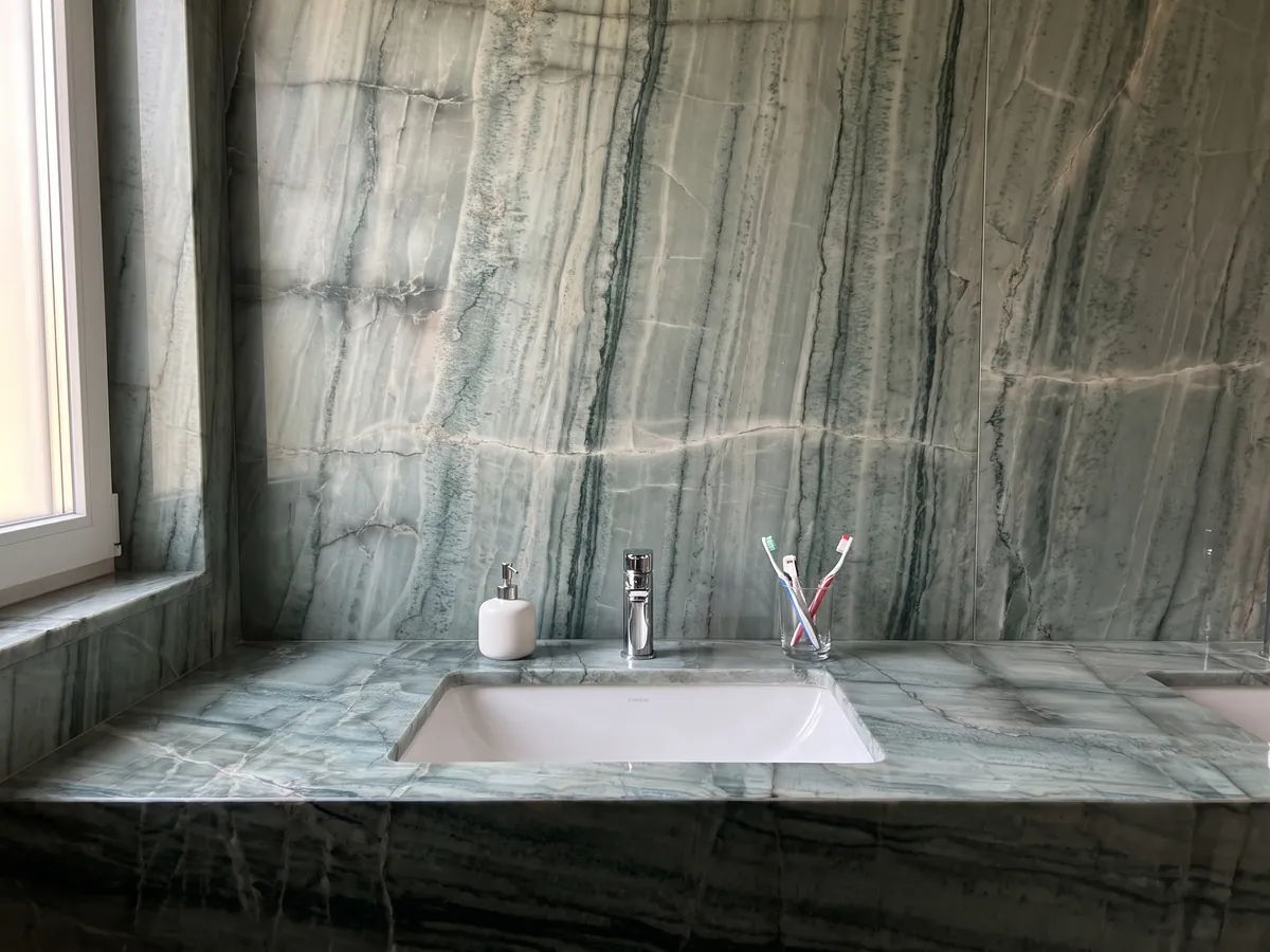 Bathroom vanity top and wall in green Da Vinci quartzite with a white sink and chrome fixtures: grayish green with a grid of dark vertical veins and light bands