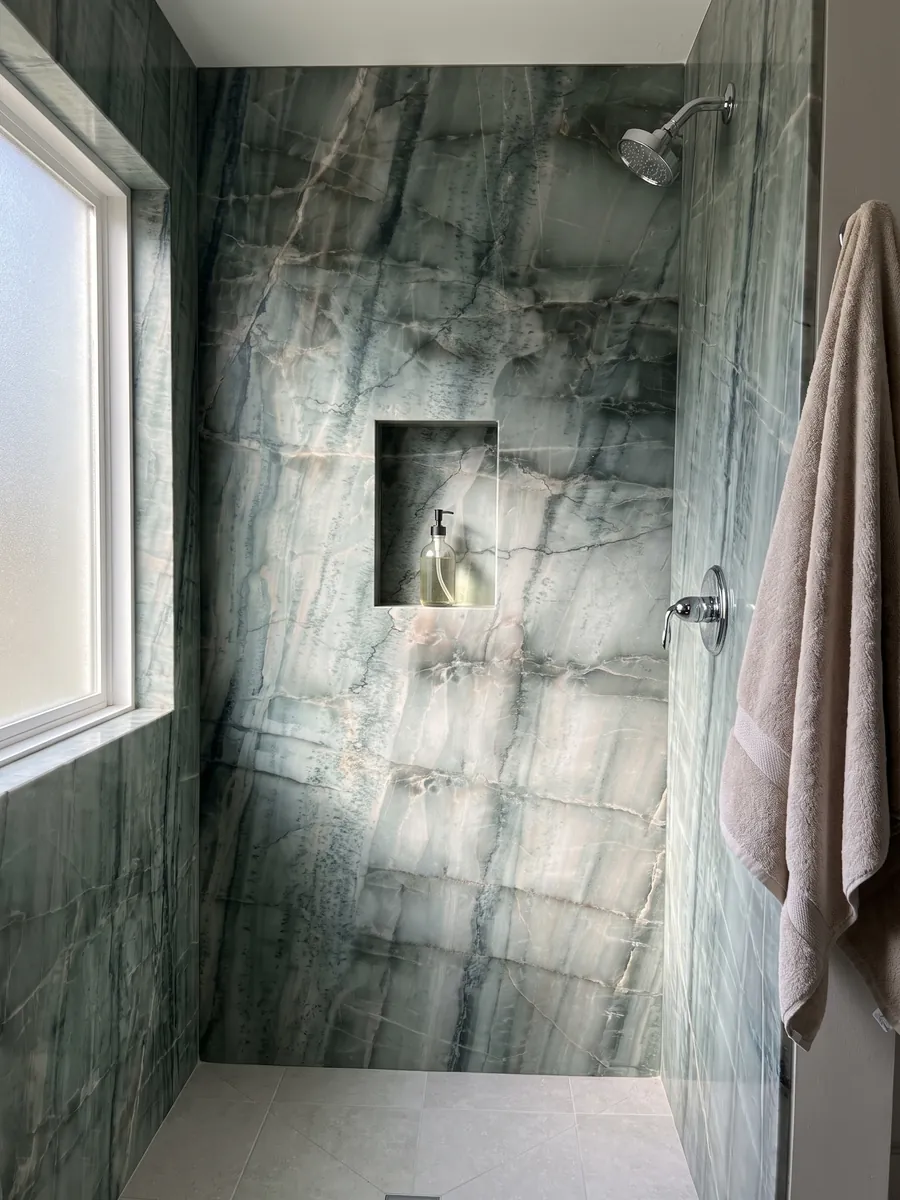 Shower clad in full green Da Vinci quartzite slabs with a recessed niche: grayish green with a grid of dark vertical veins and light bands
