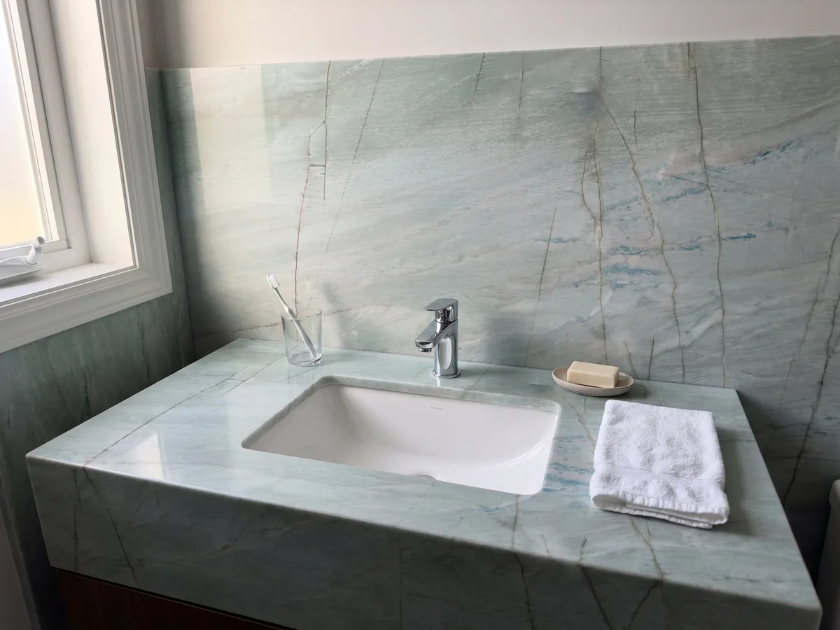 Vanity top and bathroom wall in Emerald Green quartzite with a white sink and chrome faucet: light sea green with fine vertical dark lines and small blue glints