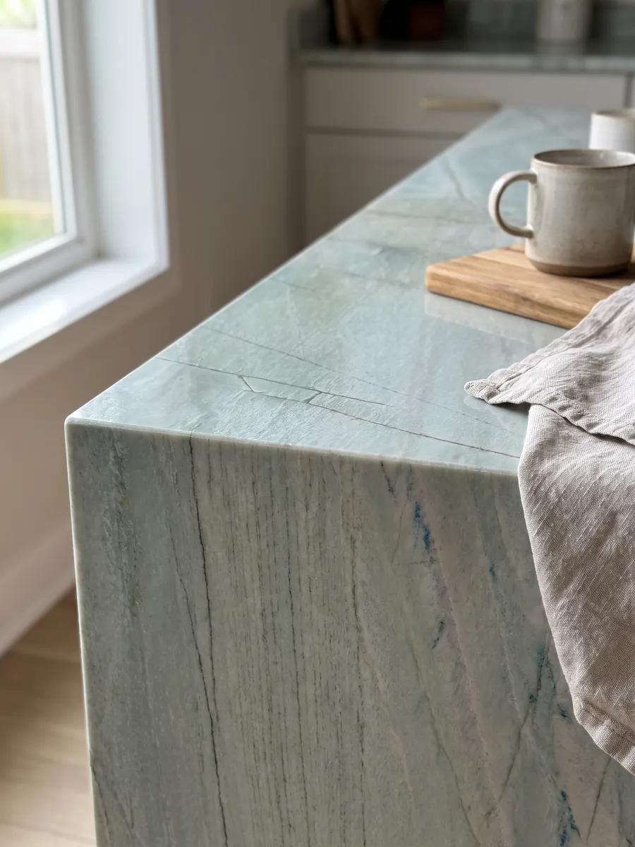 Straight edge of an Emerald Green quartzite kitchen countertop with the veining running over the edge: light sea green with fine vertical dark lines and small blue glints