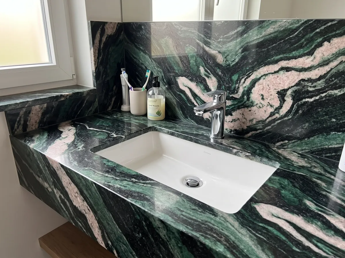 Vanity top and bathroom wall in Lapponia Green quartzite with a white sink and chrome faucets: emerald green and black with large pinkish white waves