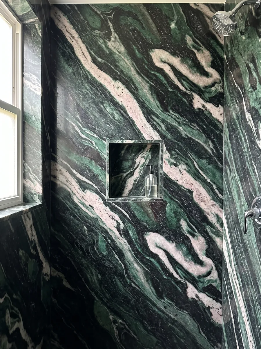 Shower clad in full Lapponia Green quartzite slabs with a recessed niche: emerald green and black with large pinkish white waves