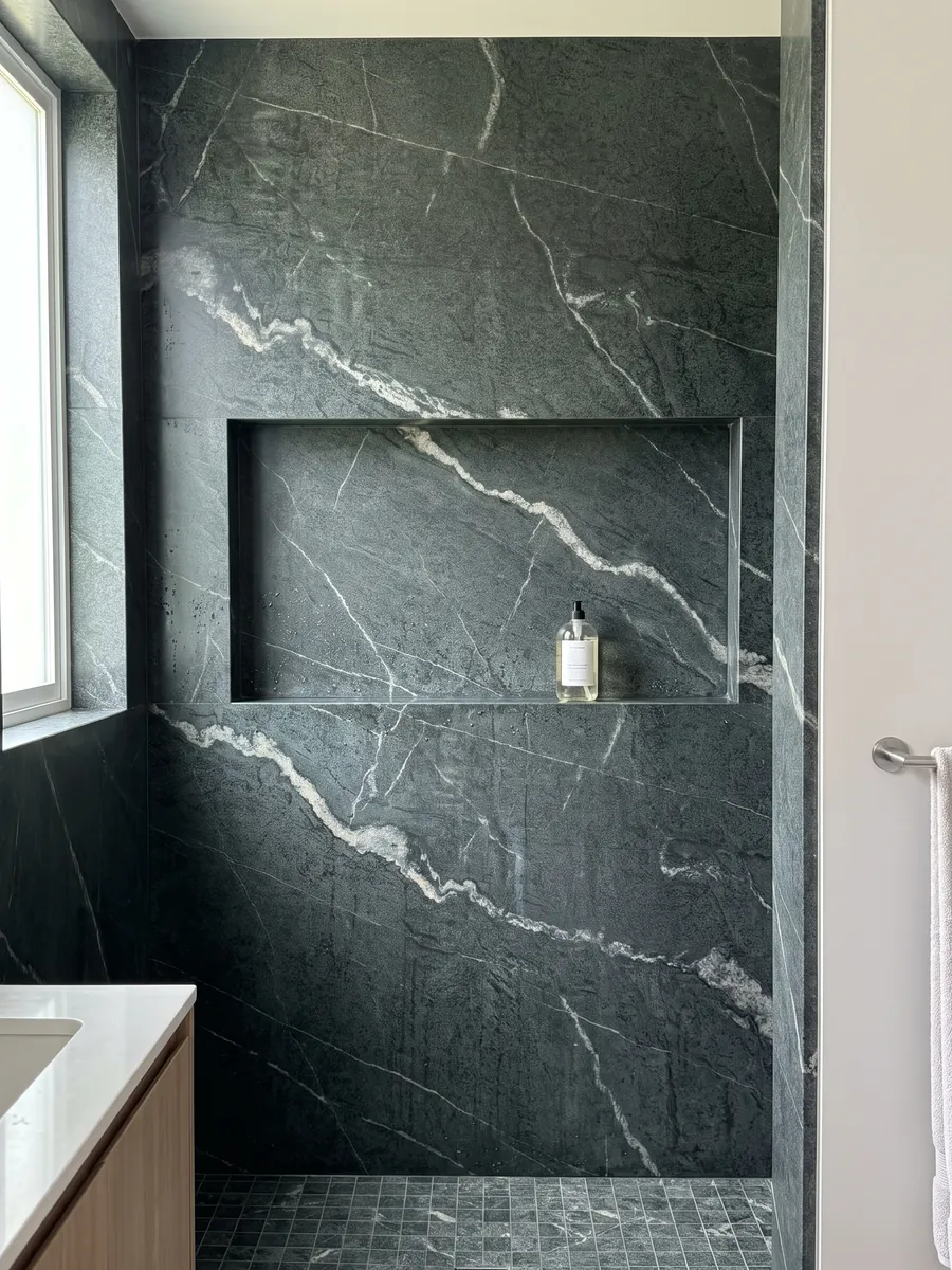 Shower clad in full slabs of green Pietra Ollare quartzite with a recessed niche: granular near-black green with a wandering white vein