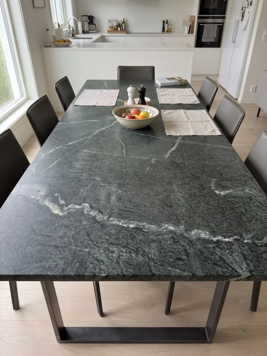 Dining table with a green Pietra Ollare quartzite top on a steel base: granular near-black green with a wandering white vein